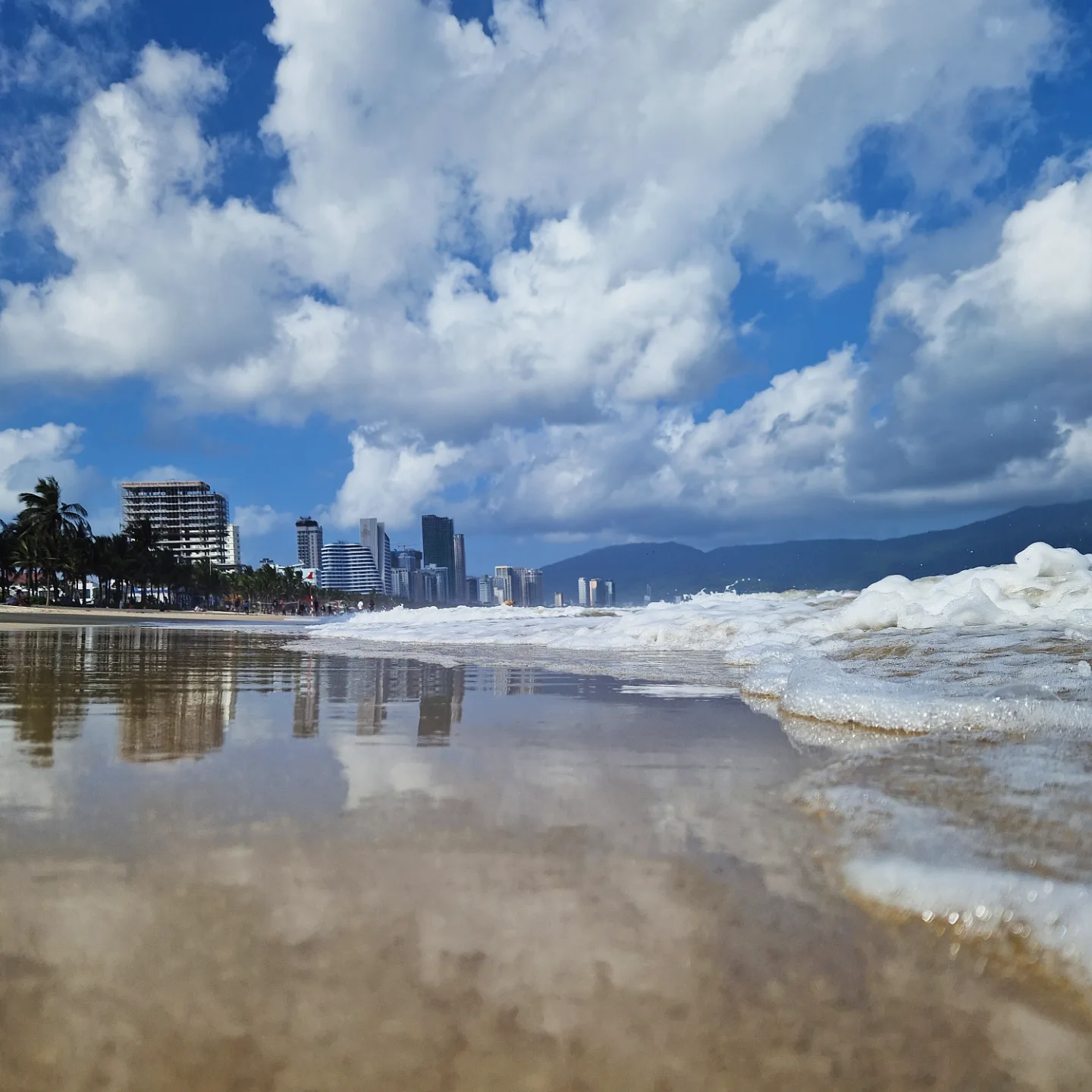 My Khe shoreline with the Da Nang skyline and Son Tra reflected in wet sand