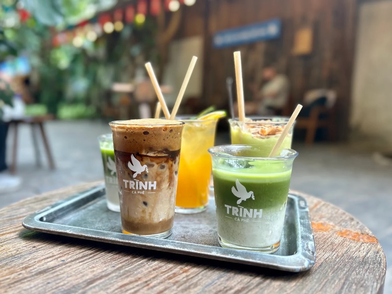 A metal tray of Trịnh Cà Phê drinks: Vietnamese coffee, matcha, avocado and citrus, dove-logo glasses