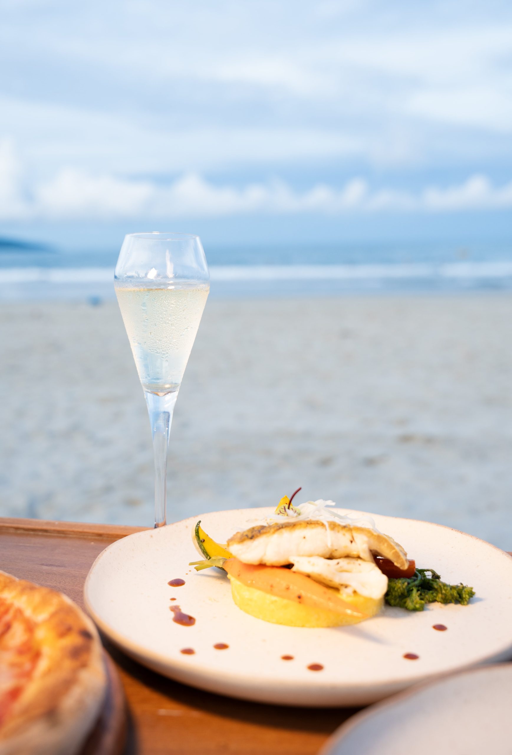 Plated fish course with a glass of sparkling wine on the beach at dusk