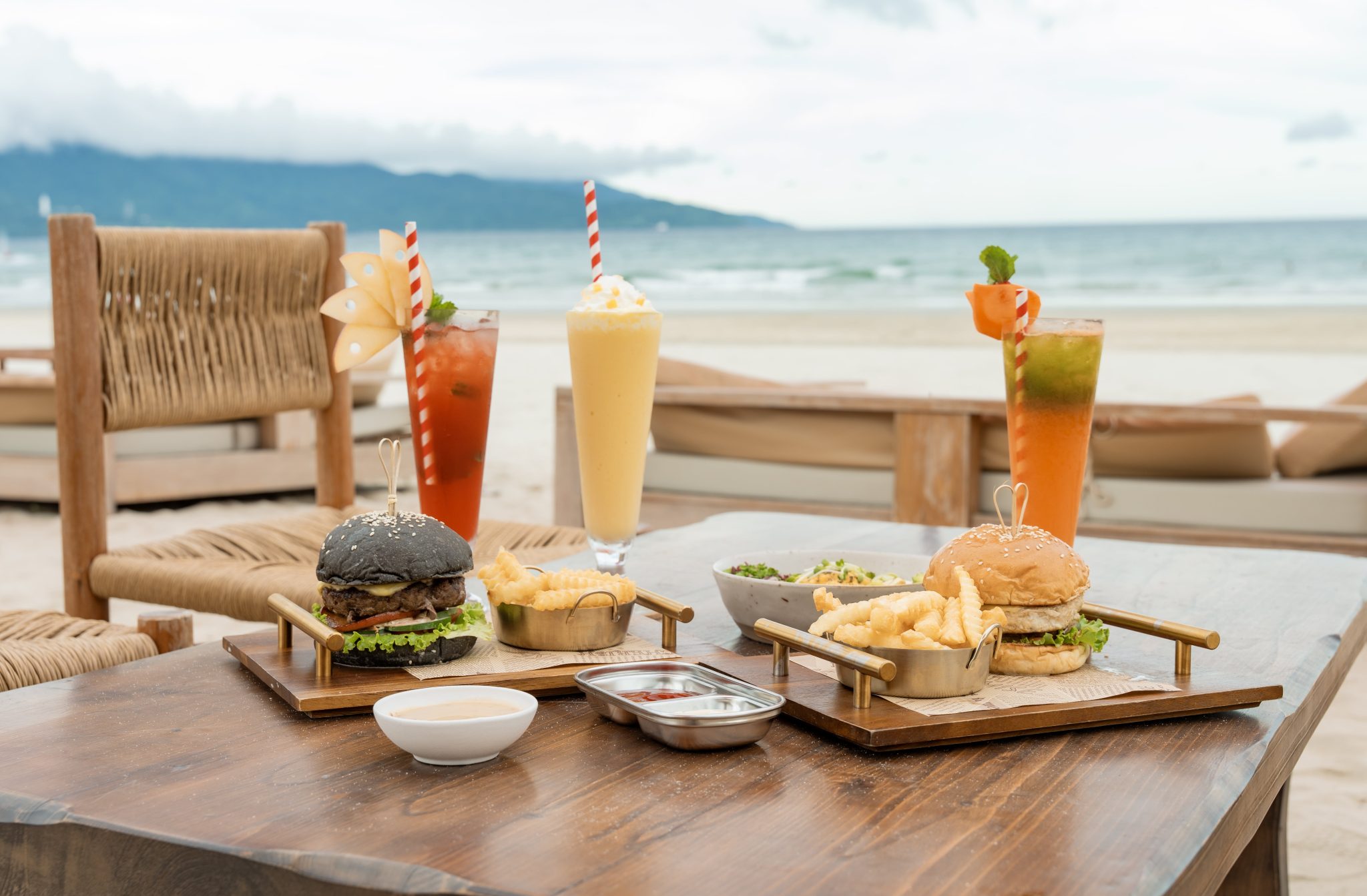Beachfront table of burgers, fries and fresh drinks with the sea behind