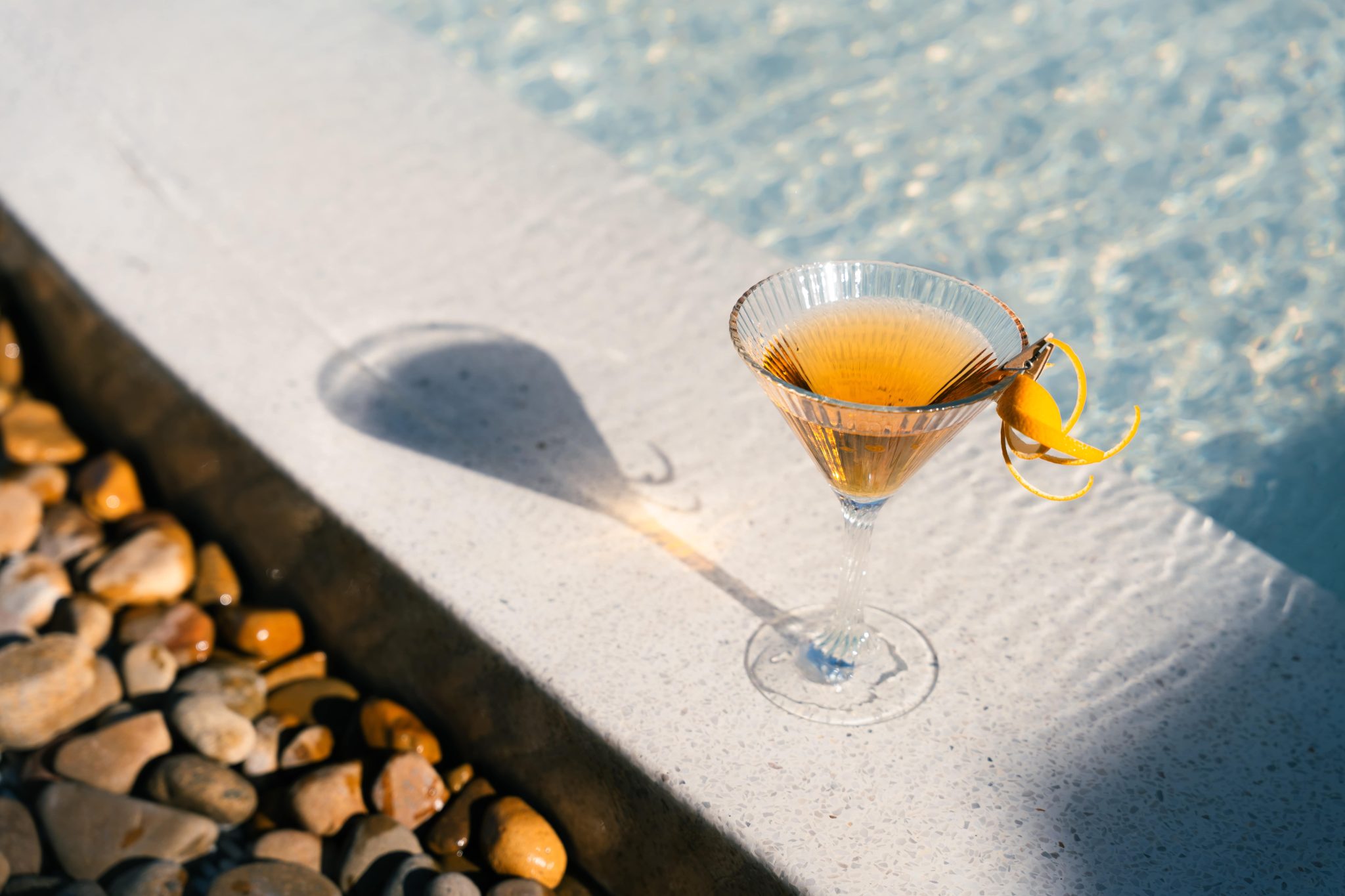 A martini garnished with citrus peel on the edge of the pool