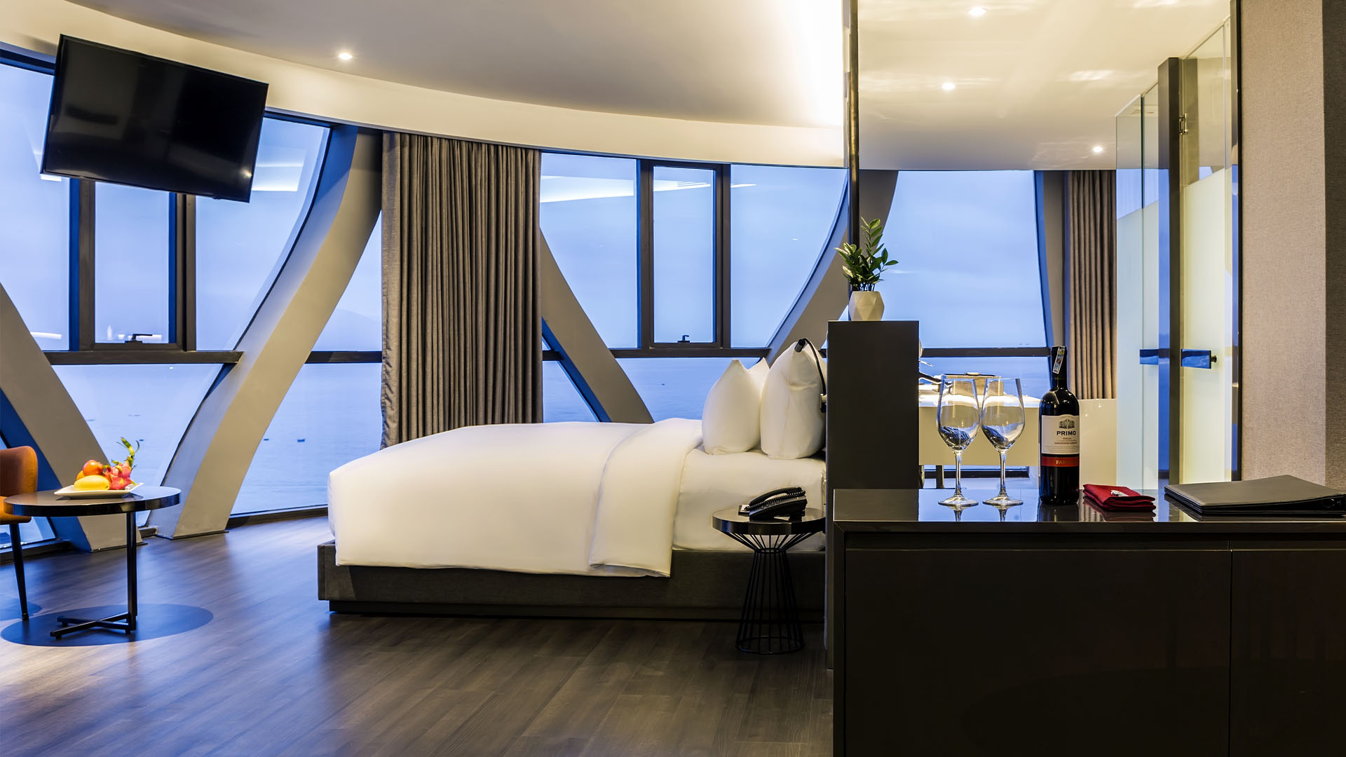 Corner ocean-view suite with curved floor-to-ceiling glass braced by sculptural ribs