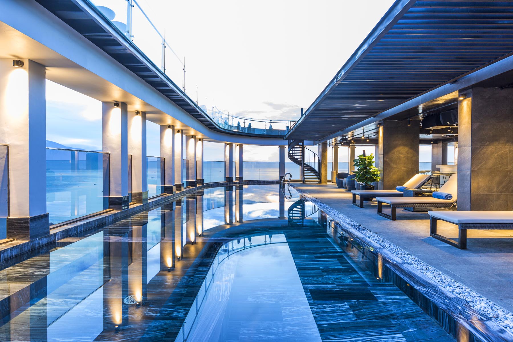 Rooftop infinity pool at dusk with a colonnade and sea view
