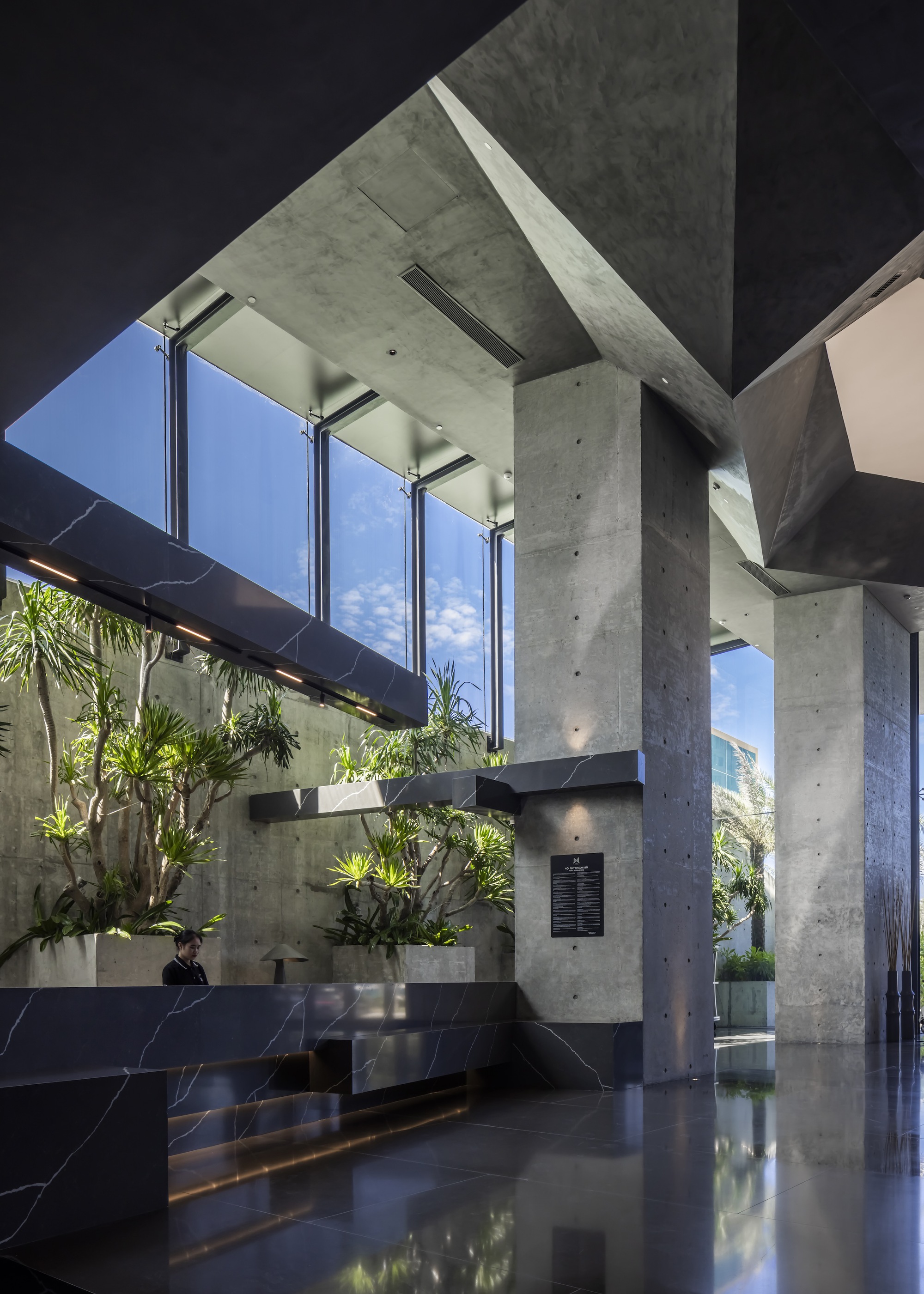 The concrete-and-marble lobby with indoor trees under angular skylights