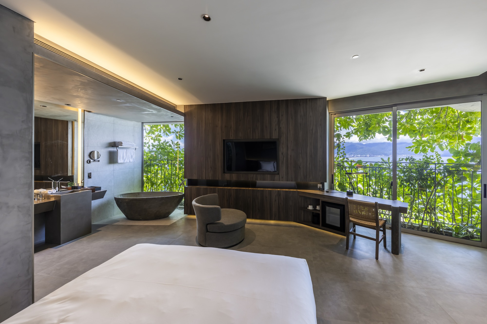 Guest room with a stone tub and balcony onto greenery and the coast