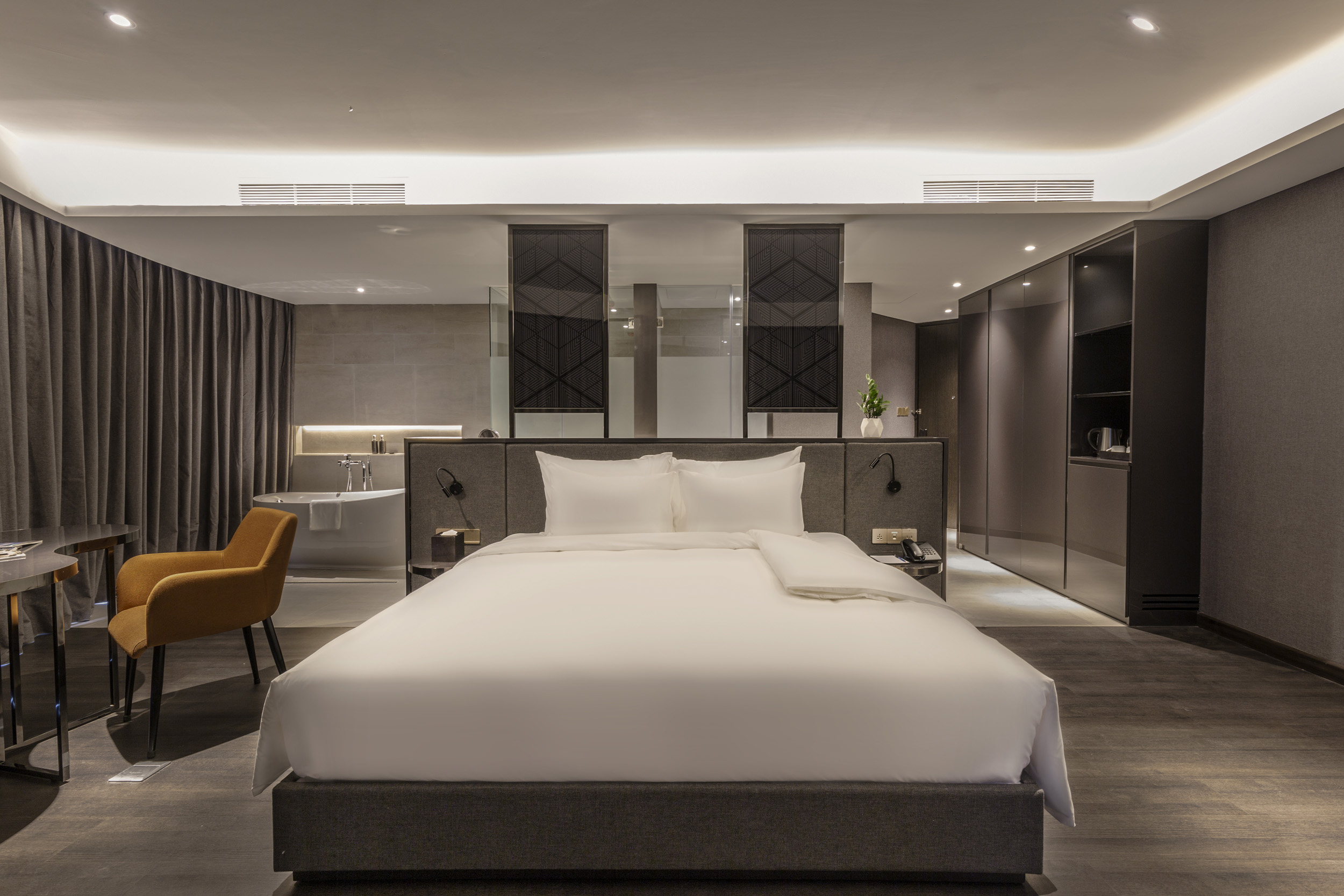 Modern suite with a king bed and freestanding tub in a gray-and-timber palette