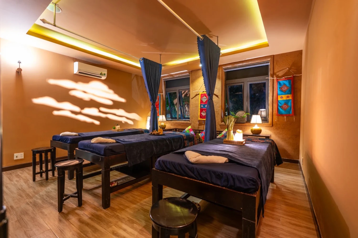 A warm, lamp-lit twin massage treatment room with ethnic textiles at Luxury Herbal Spa